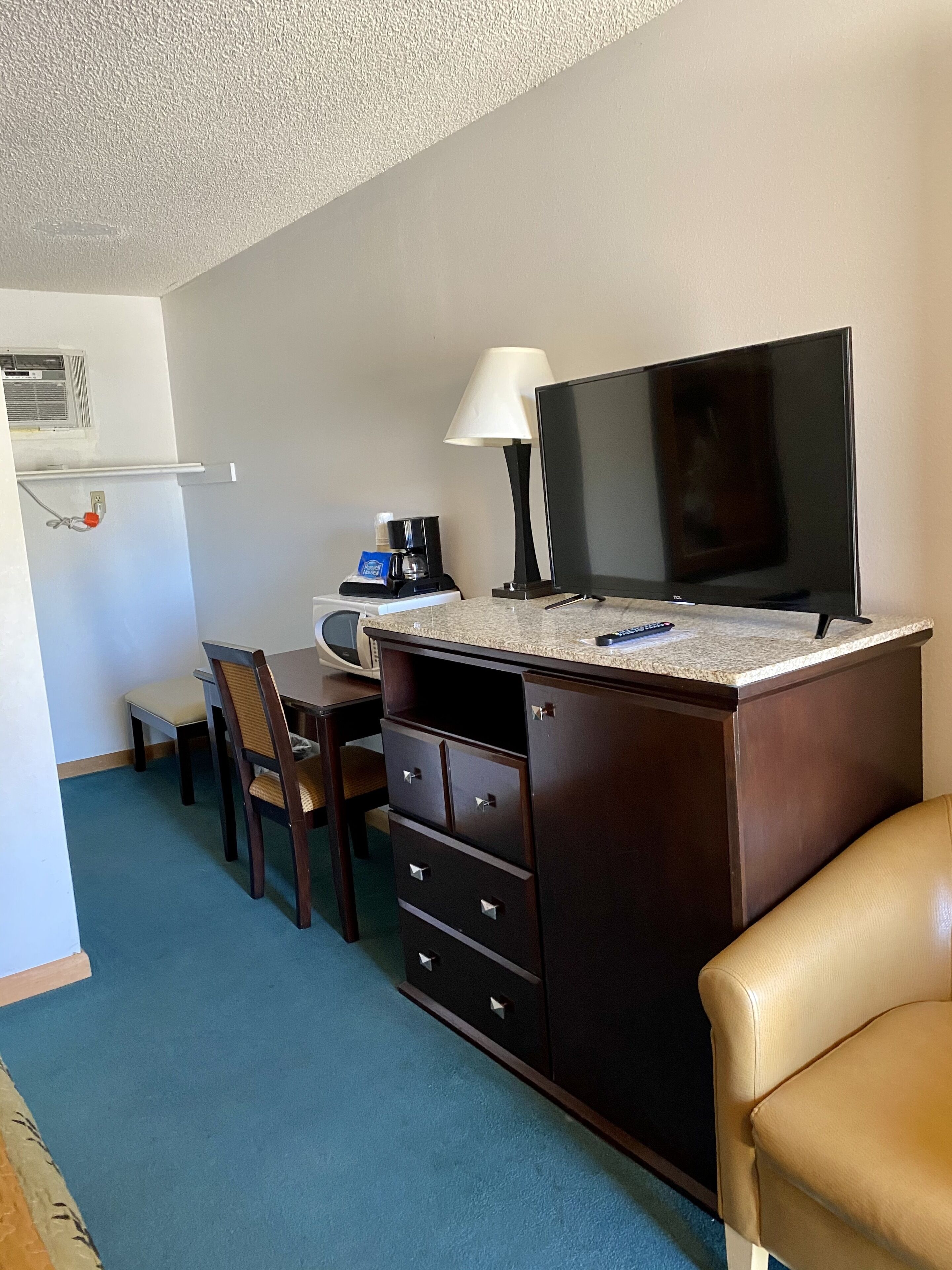 A small room with a desk, chair, TV, lamp, and a coffee maker.
