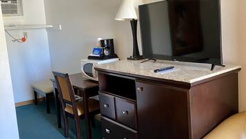 A small room with a desk, chair, TV, lamp, and a coffee maker.