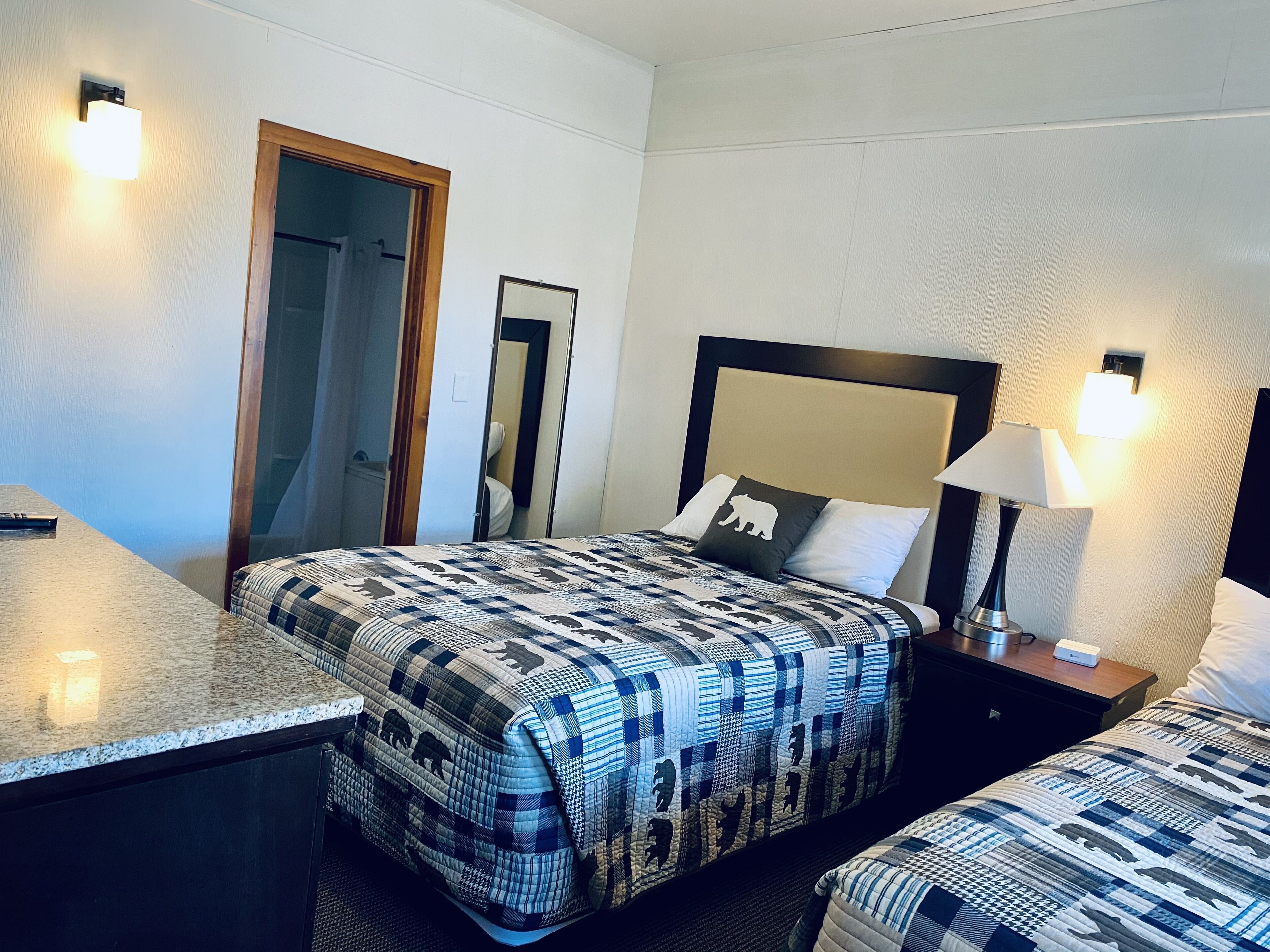 A hotel room with a bed, a bedside table, a lamp, a mirror, and a door.