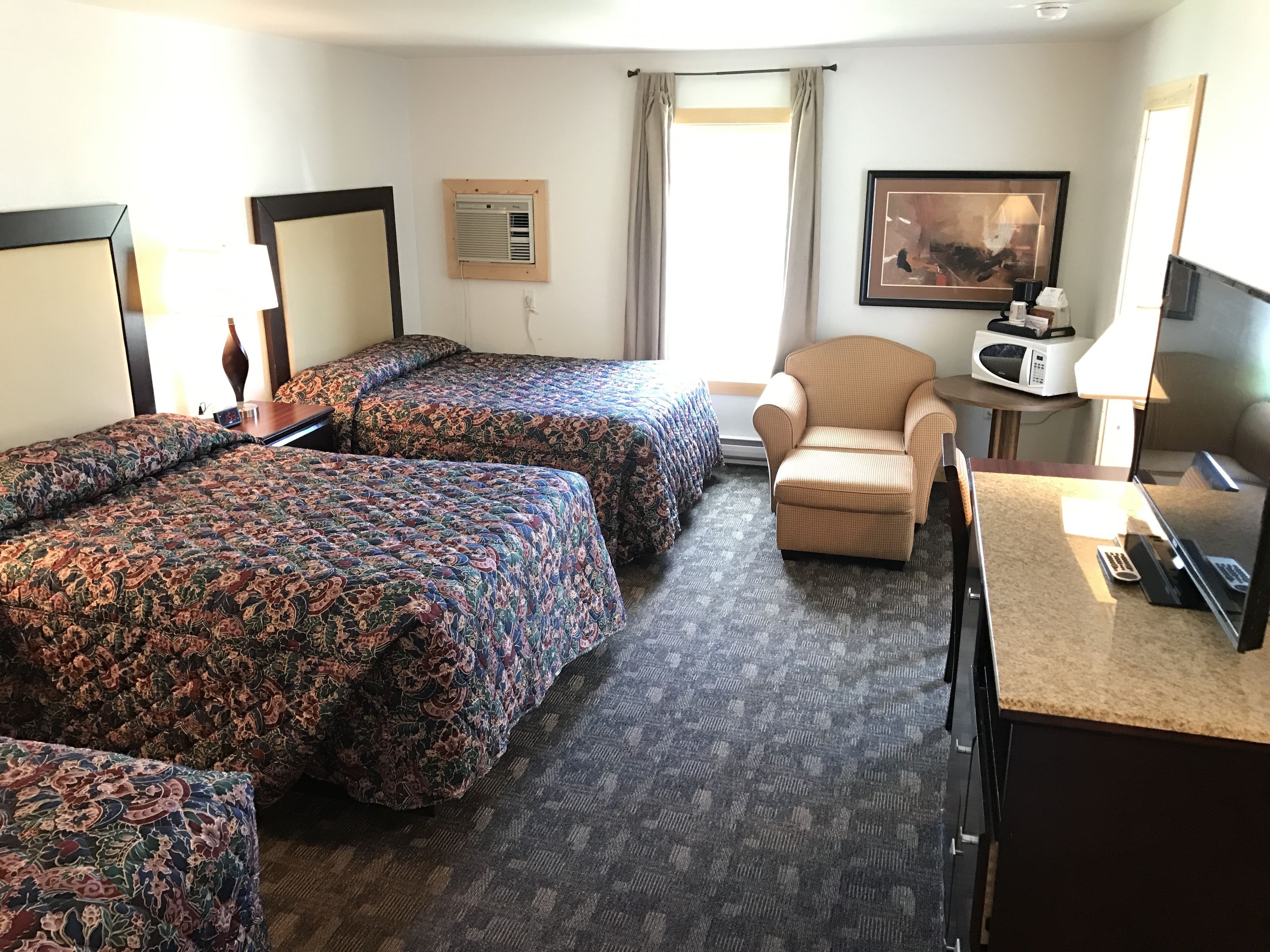 Une chambre d’hôtel avec deux lits, une chaise, un bureau, un four à micro-ondes et un tableau au mur.