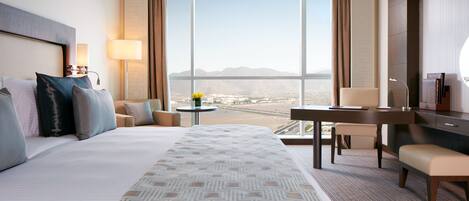 A hotel room with a large bed, a desk, a chair, and a view of the desert.