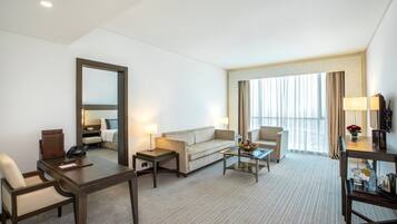 Habitación de hotel con sofá, sillones, una mesa de centro, escritorio, espejo y televisor.