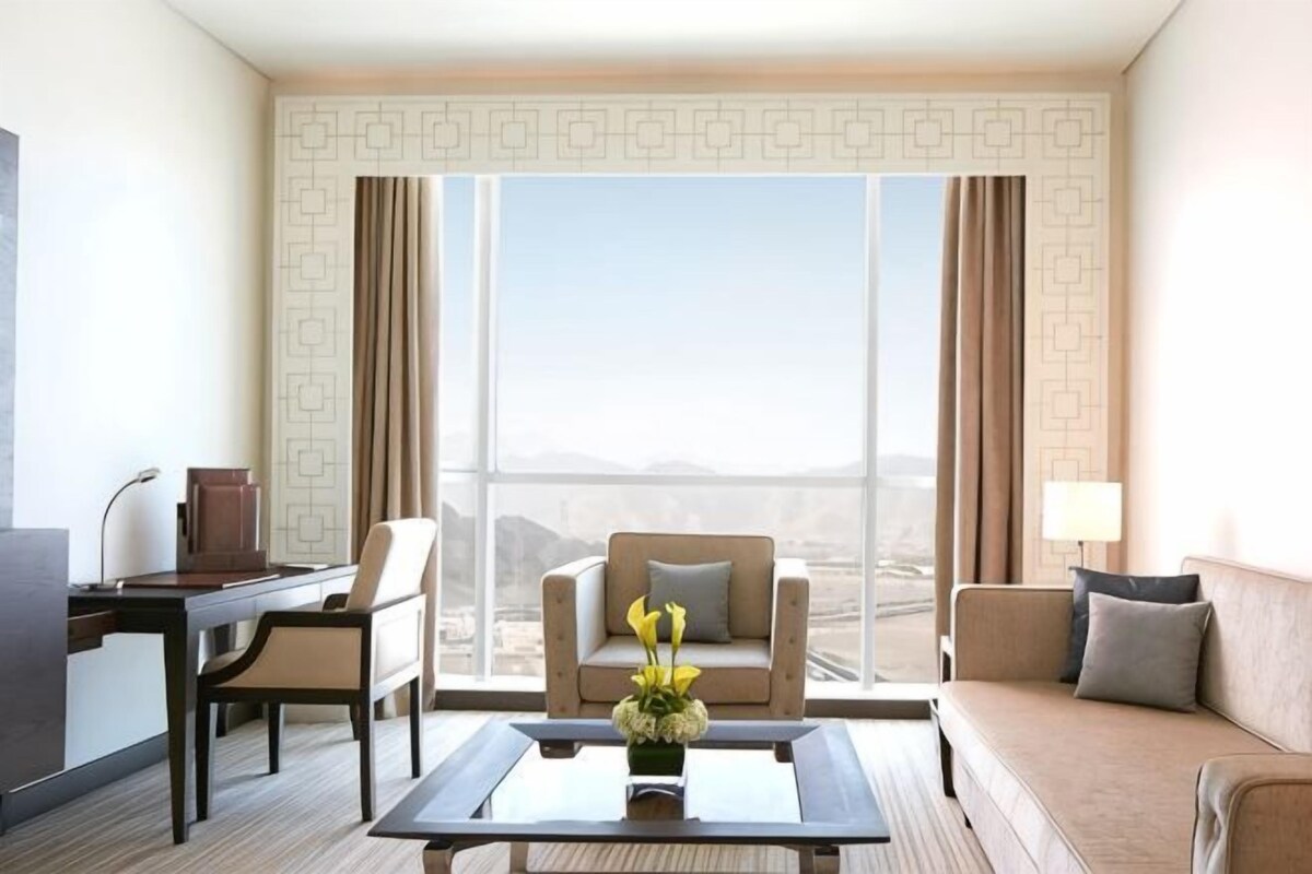 A hotel room with a large window, a desk, a sofa, and a coffee table.