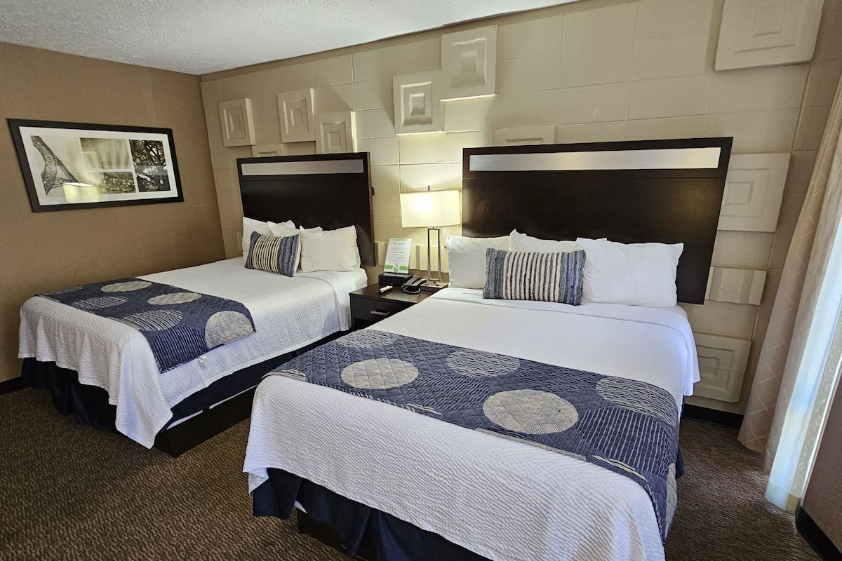 A hotel room with two beds, each with a headboard, a nightstand, a lamp, and a framed picture on the wall.