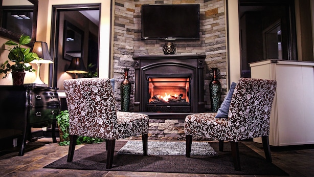 A cozy living room with a fireplace, two patterned armchairs, a television mounted above the fireplace, and a potted plant. - The Landmark Hotel (Pikeville)