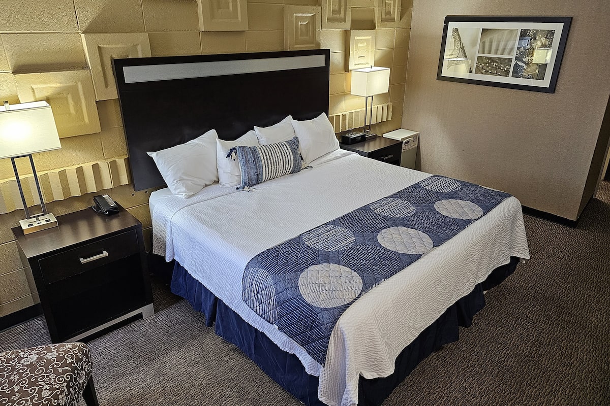 A hotel room with a large bed, a nightstand with a lamp, a dresser, and a carpeted floor.