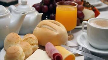 A breakfast setting with bread rolls, cheese, ham, grapes, and orange juice.