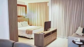 Una habitación de hotel con una cama, un televisor sobre una consola de madera, un sofá y una mesita.