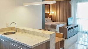 Una habitación de hotel moderna con kitchenette, una cama, un televisor y un ventanal grande.