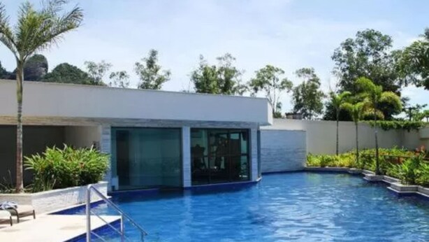 Una piscina con un edificio moderno al fondo, rodeada de vegetación.