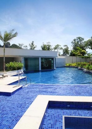 Una piscina con un edificio moderno al fondo, rodeada de vegetación.