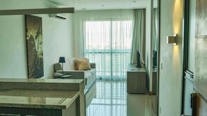 Una habitación de hotel moderna con sofá, una mesita, televisor y balcón con cortinas.