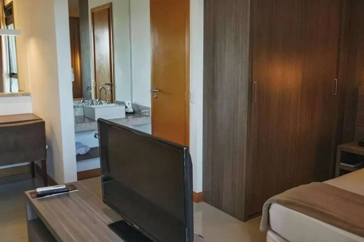 Habitació d'hotel amb un llit, una televisió, un armari de fusta i un bany amb un lavabo i un mirall.