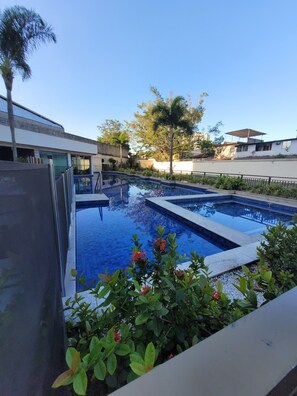 A swimming pool with a tiled deck, surrounded by greenery and a clear sky. - Samba Rio Grand Midas (Rio de Janeiro)