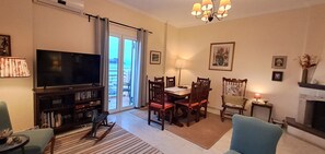 Una sala de estar con televisor, estanterías, una mesa de comedor con sillas, chimenea y un balcón con cortinas.