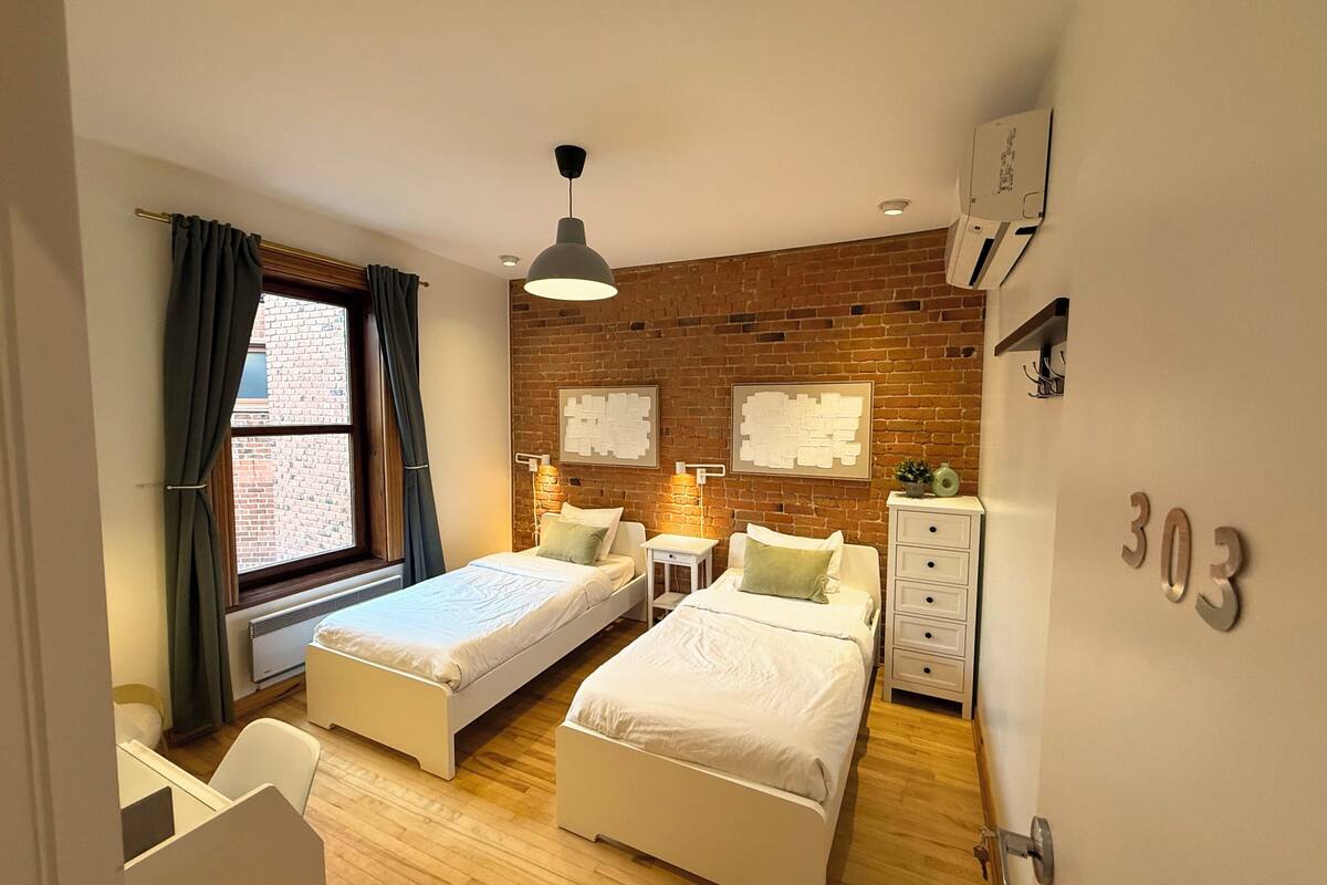 A modern bedroom with two single beds, a desk, and a dresser.
