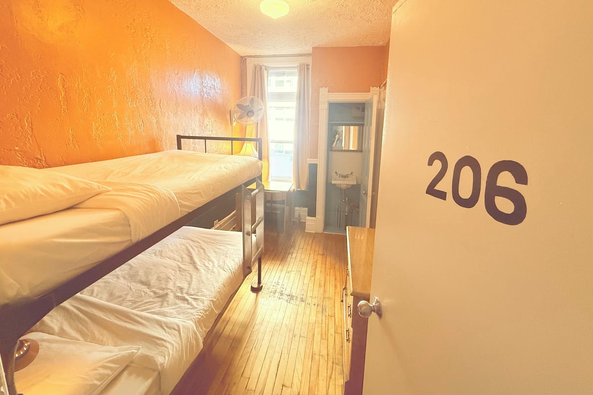 A room with bunk beds, a door labeled 206, a fan, and a window with curtains.