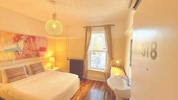 A bedroom with a bed, bedside lamps, a window with curtains, a radiator, and a number on the wall.