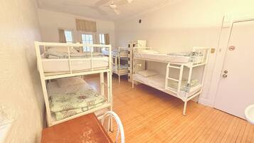 A room with bunk beds, a desk, a chair, a ceiling fan, and a door with a number.