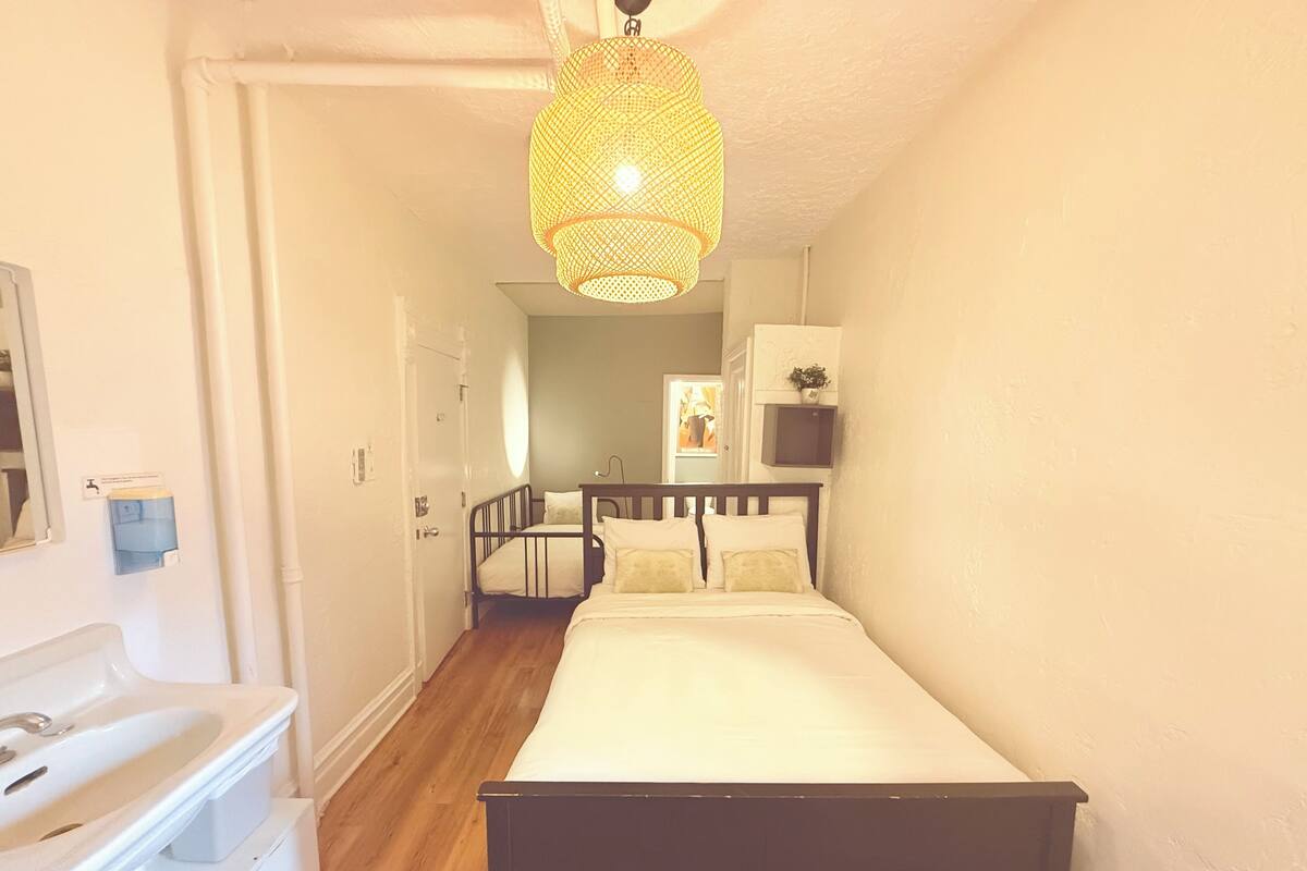 A narrow hallway with a bed, a sink, and a hanging light fixture.