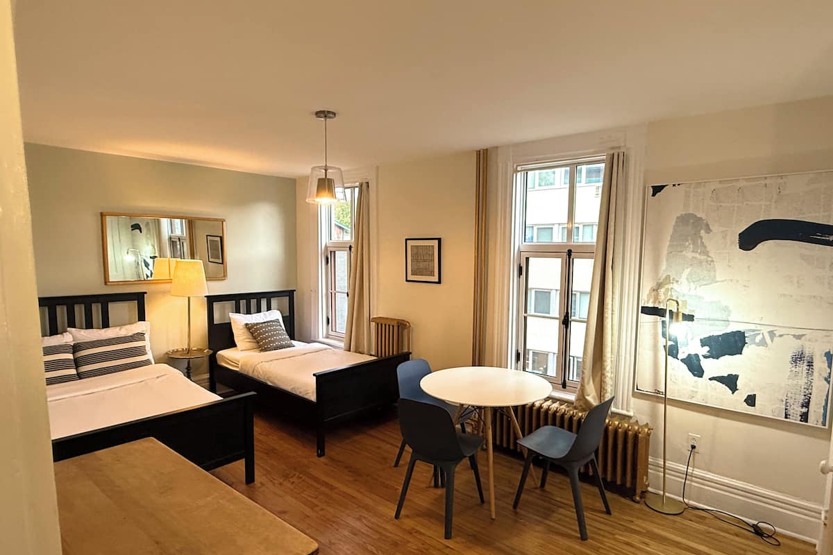A hotel room with two beds, a dining table with chairs, a large window with curtains, and a map on the wall.