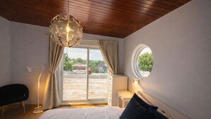 Un dormitorio con cama, un espejo redondo, una lámpara de techo y vistas a través de una ventana.