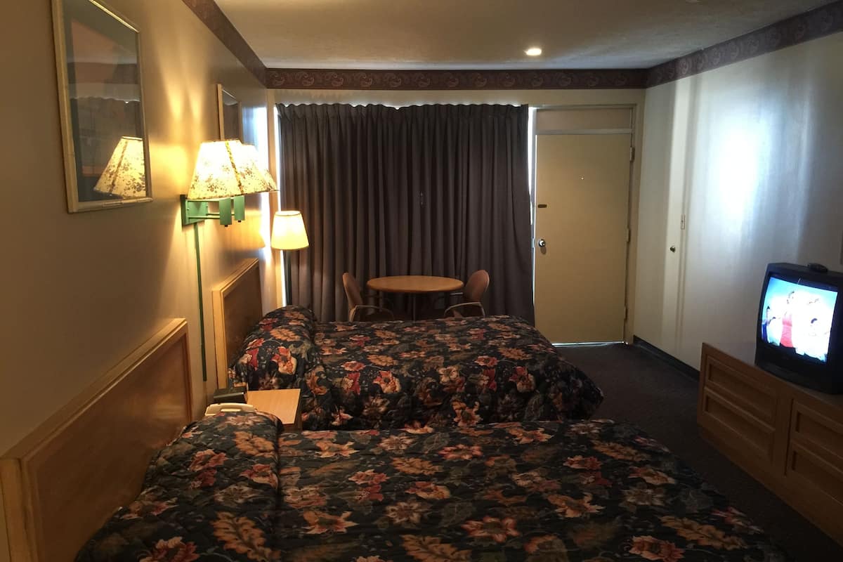 A hotel room with a double bed, two bedside lamps, a television, a small table, and a chair.