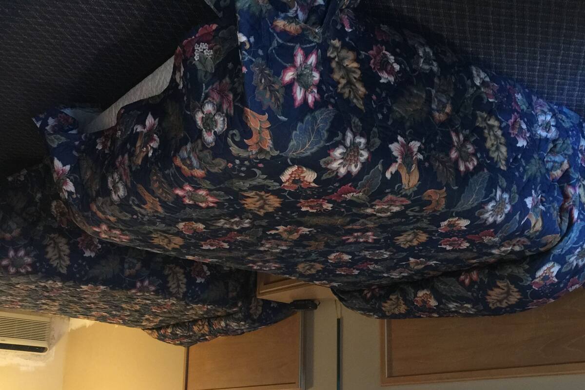 A room with a floral-patterned bedspread, a wall-mounted light fixture, and framed artwork.
