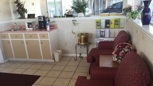 A living room with a red sofa, a coffee machine, a trash bin, and a small table with a vase of flowers. - Ashland Inn (Ashland)