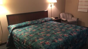 A hotel room with a bed, a chair, a nightstand, and a lamp. - Ashland Inn (Ashland)
