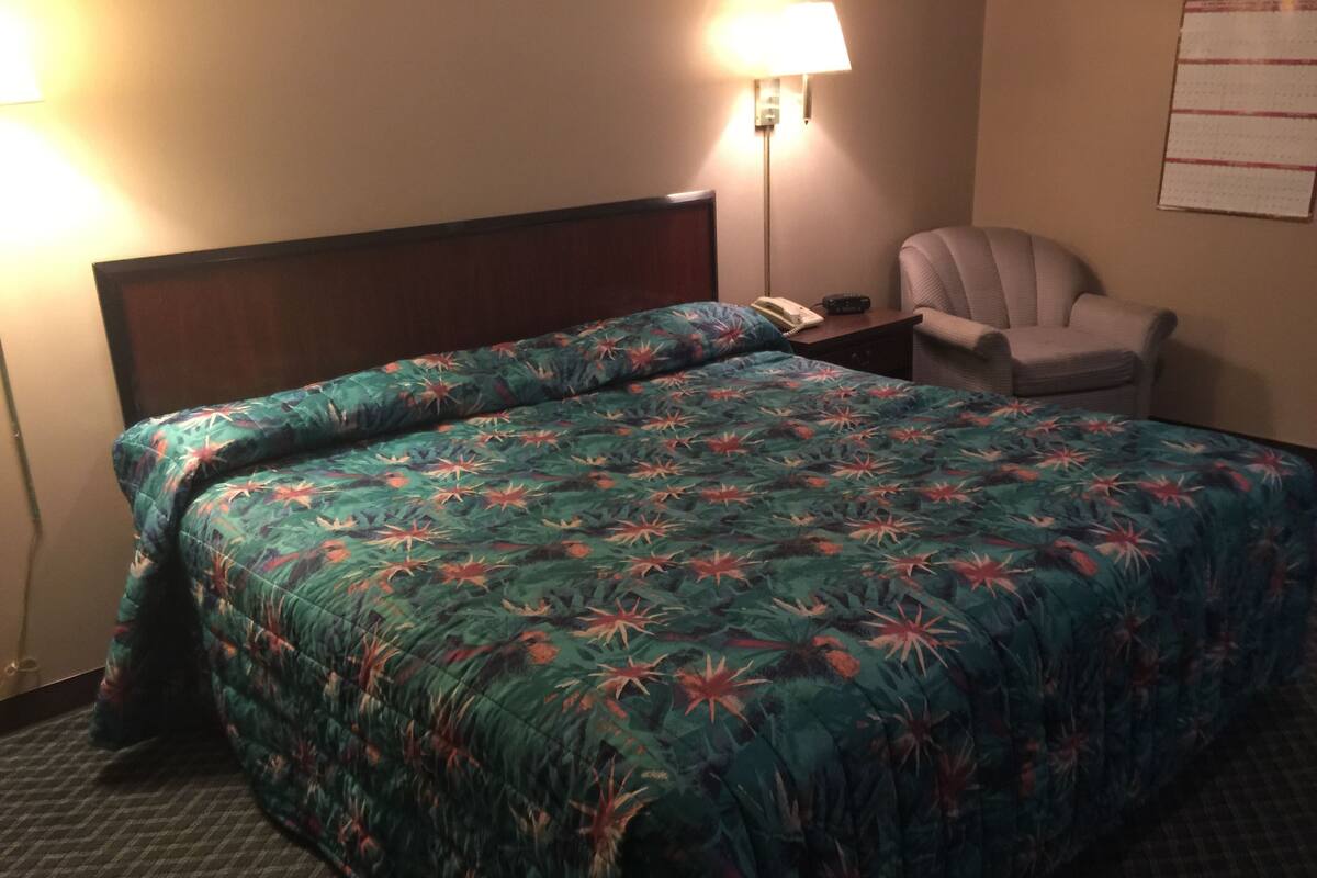 A hotel room with a bed, a chair, a nightstand, and a lamp.
