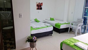 Habitación de hotel con dos camas, cada una con colcha verde y almohadas blancas. Hay una pequeña planta en maceta en el suelo y un cuadro en la pared.