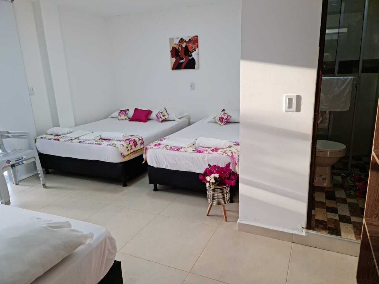 A room with two beds, a small table with a vase of flowers, and a bathroom visible through an open door.