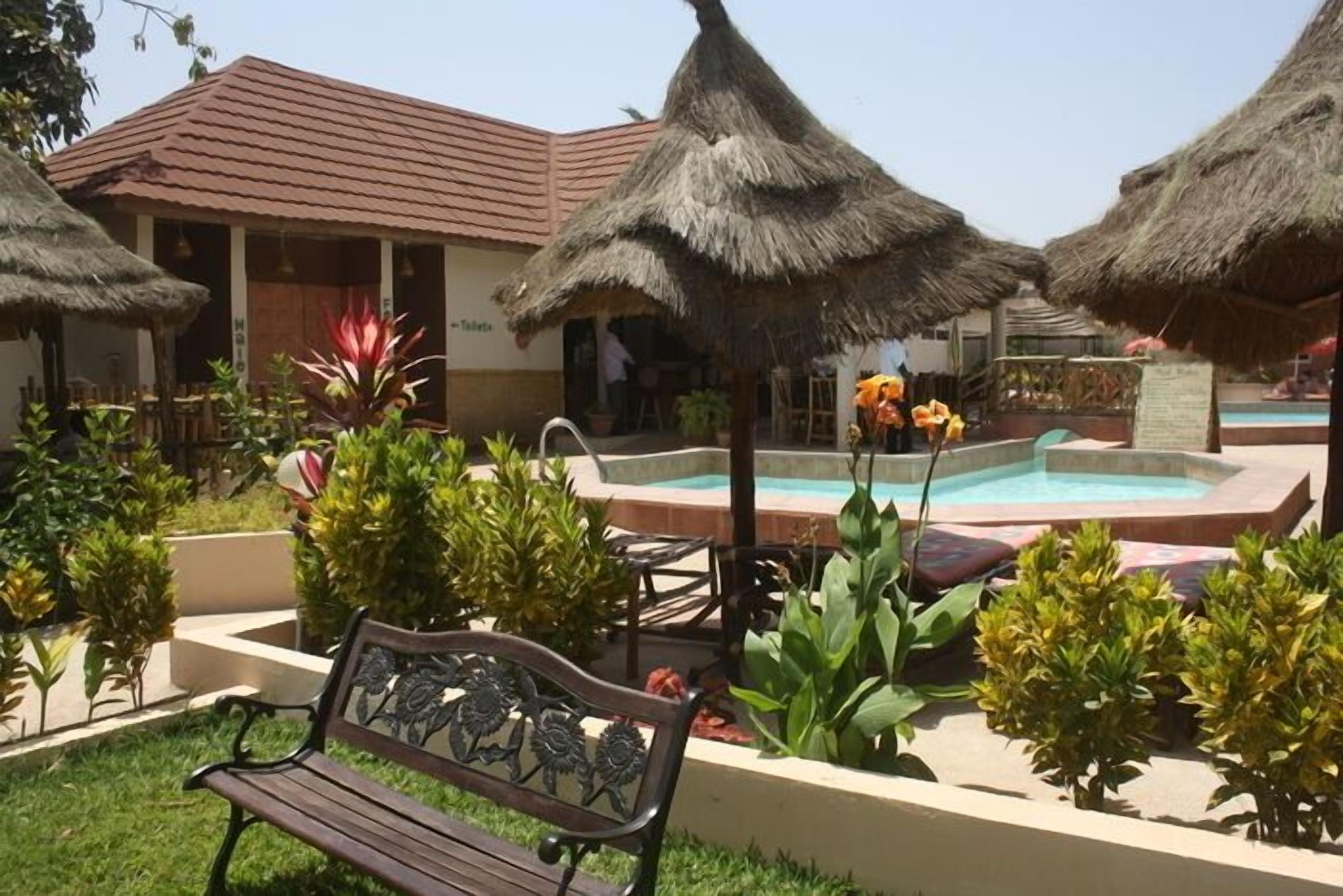 A pool area with thatched umbrellas, a bench, and potted plants.