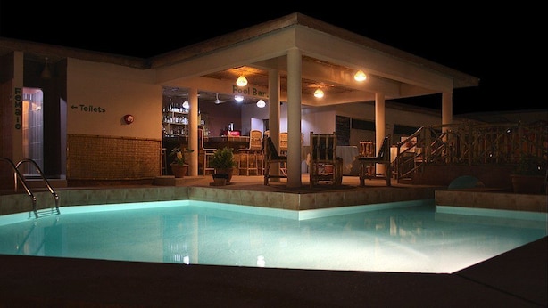 Un espace piscine doté d’un coin salon couvert, d’un bar et d’un panneau indiquant l’emplacement des toilettes.