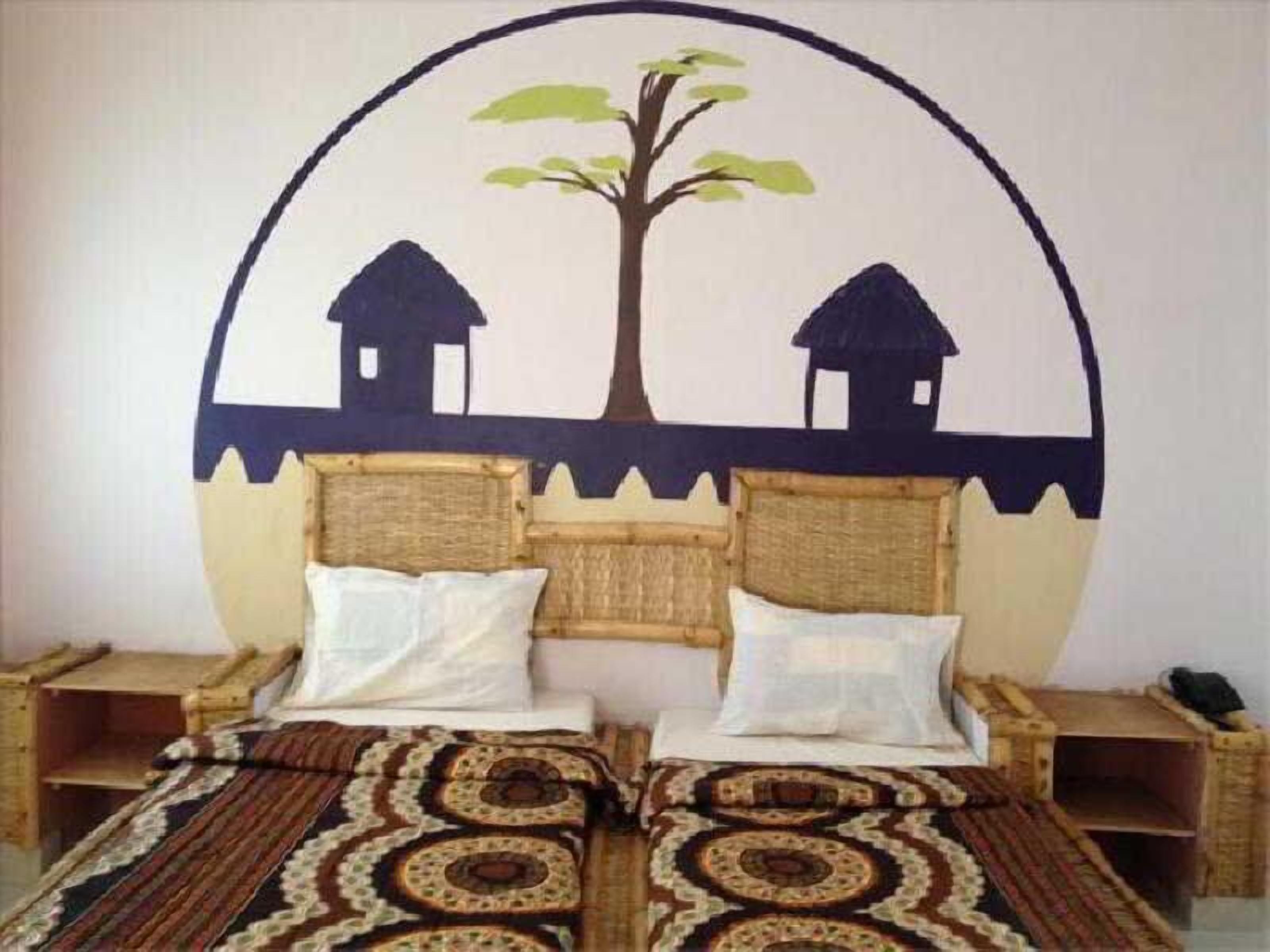 A bedroom with a bed, two pillows, a blanket, and a wall decoration of a tree and two houses.