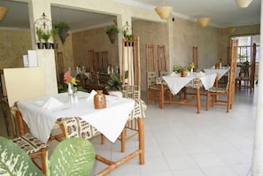 A dining area with bamboo chairs and tables, decorated with potted plants and flowers.