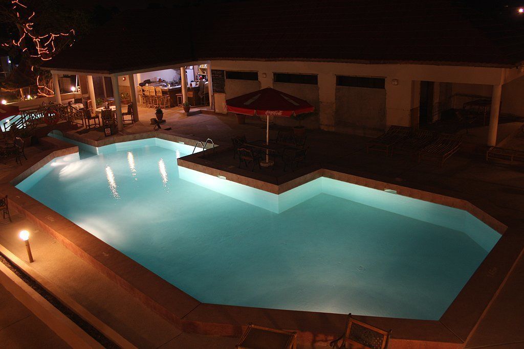 A swimming pool with a red umbrella, surrounded by outdoor seating and a building in the background.