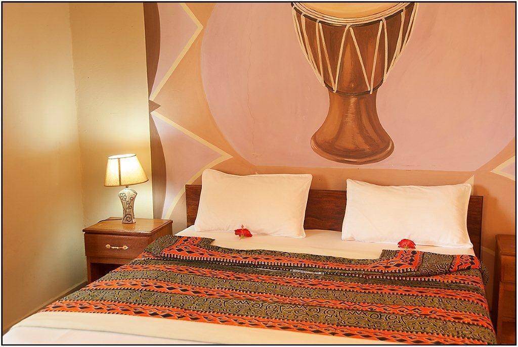 Une chambre d’hôtel avec un lit, une table de chevet avec une lampe et une fresque murale.