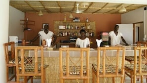 Un bar au bord de la piscine, avec des chaises et des tables en bois, un comptoir où sont exposées des bouteilles, et une enseigne au-dessus.