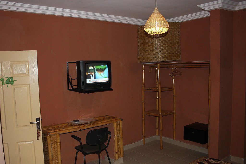 Una habitación con un televisor montado en la pared, un pequeño escritorio de madera con una silla, y una escalera de bambú apoyada contra la pared.