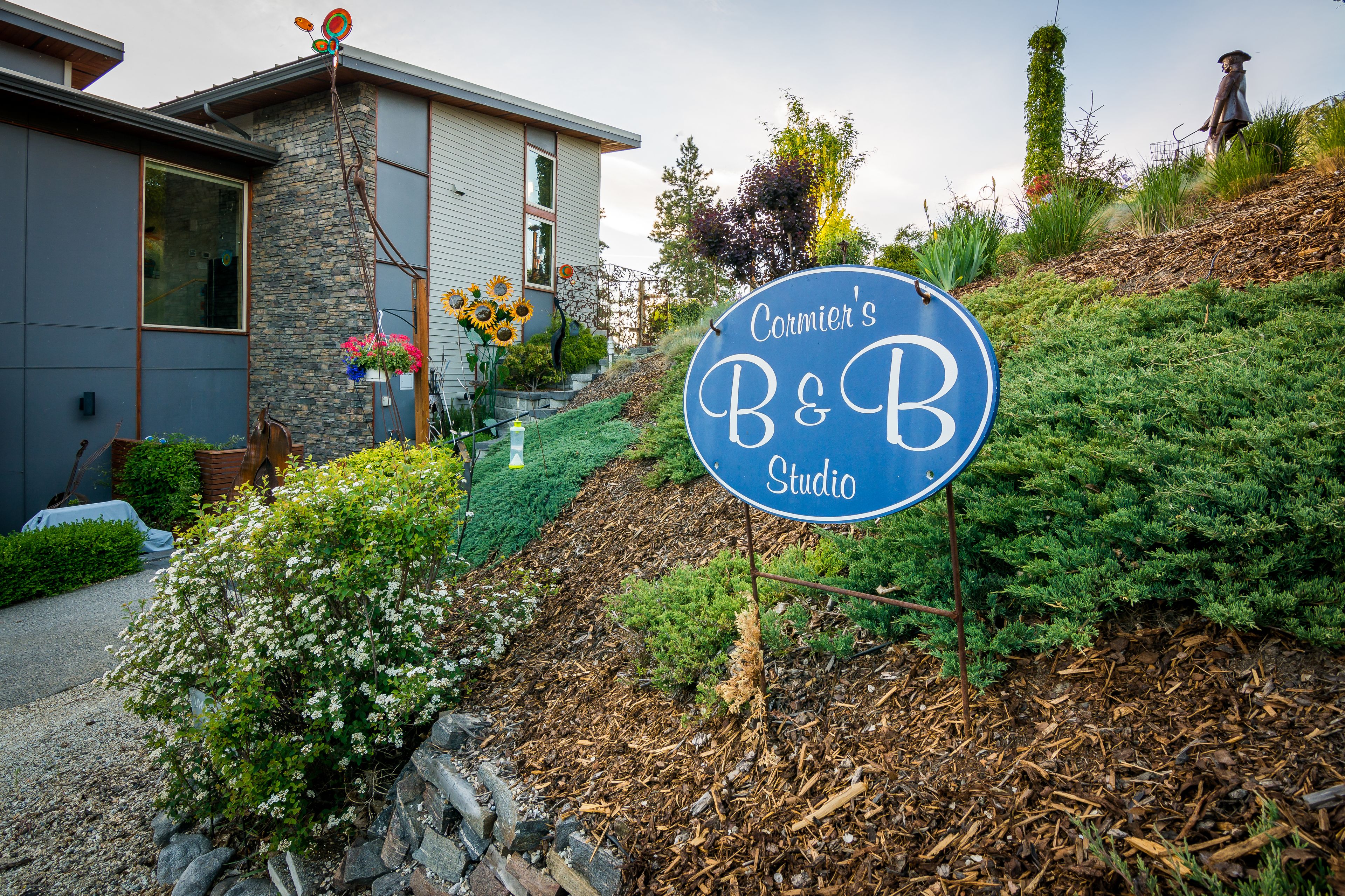 A sign for Cormier's B&B Studio with a stone facade and a garden with sunflowers.