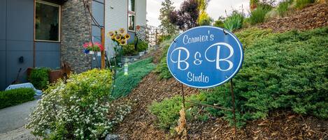 A sign for Cormier's B&B Studio with a stone facade and a garden with sunflowers.