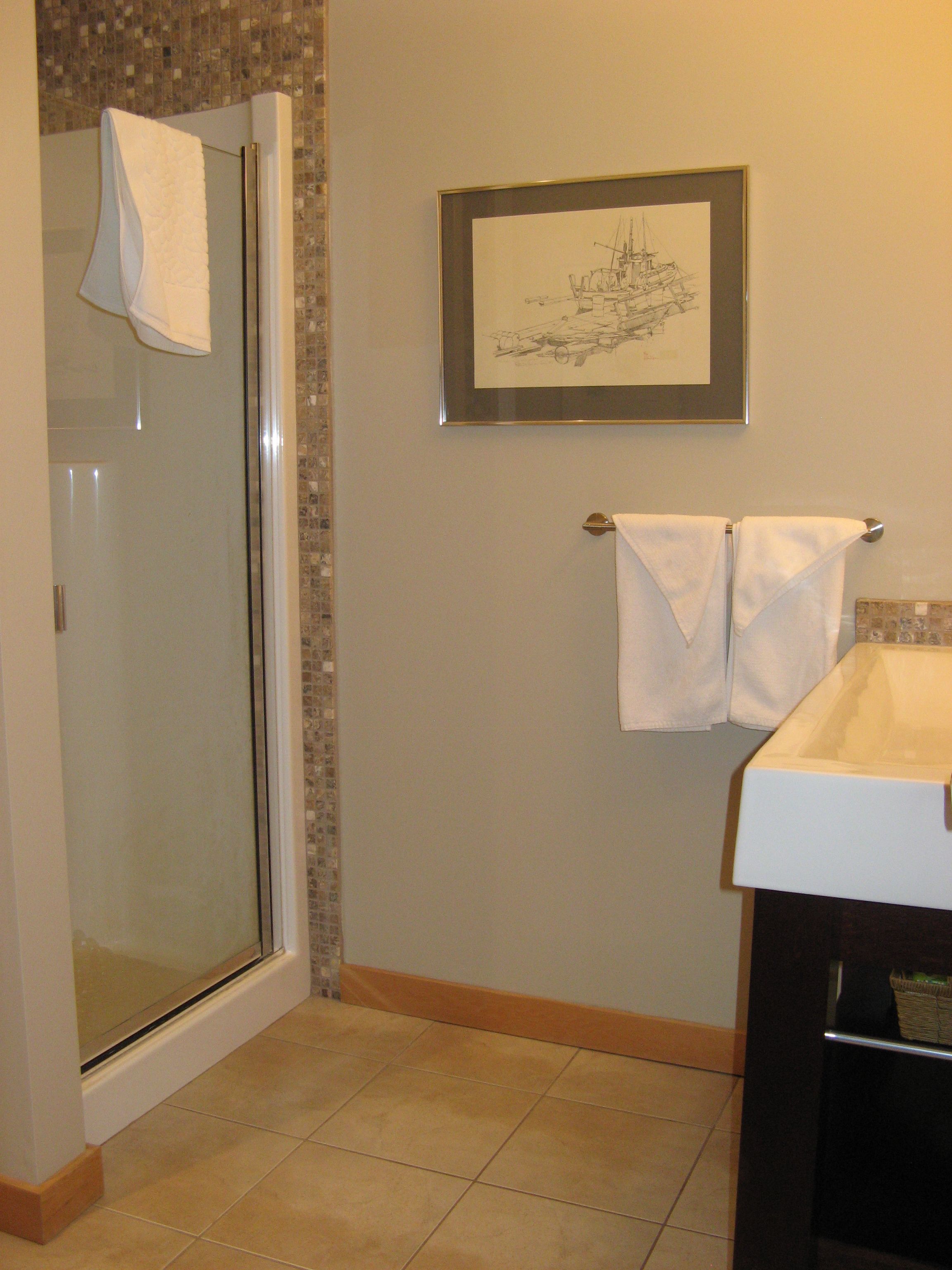 A bathroom with a glass shower enclosure, a sink, and a framed picture on the wall.
