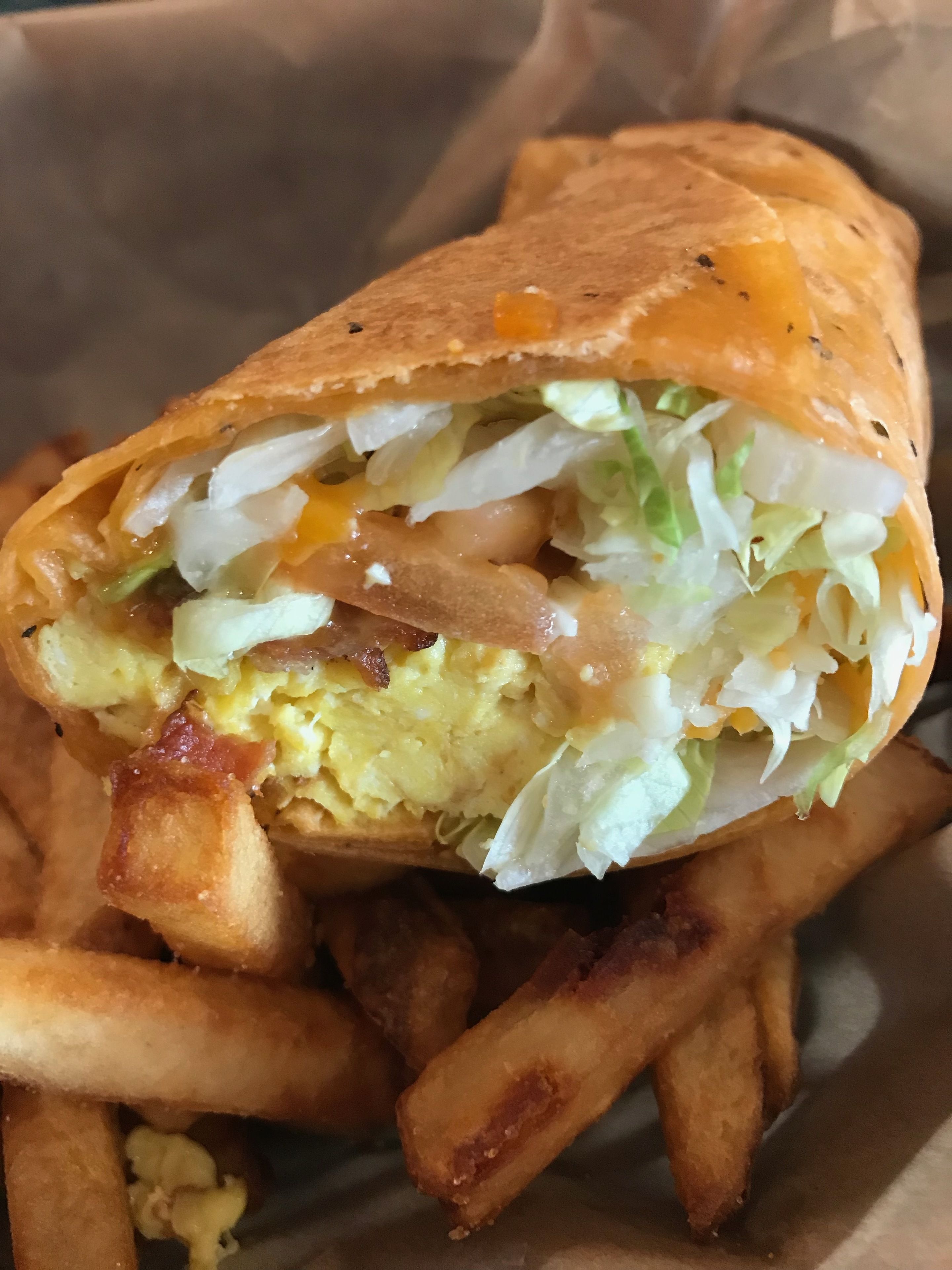 A sandwich with visible fillings such as lettuce, egg, and bacon, accompanied by a side of fries.