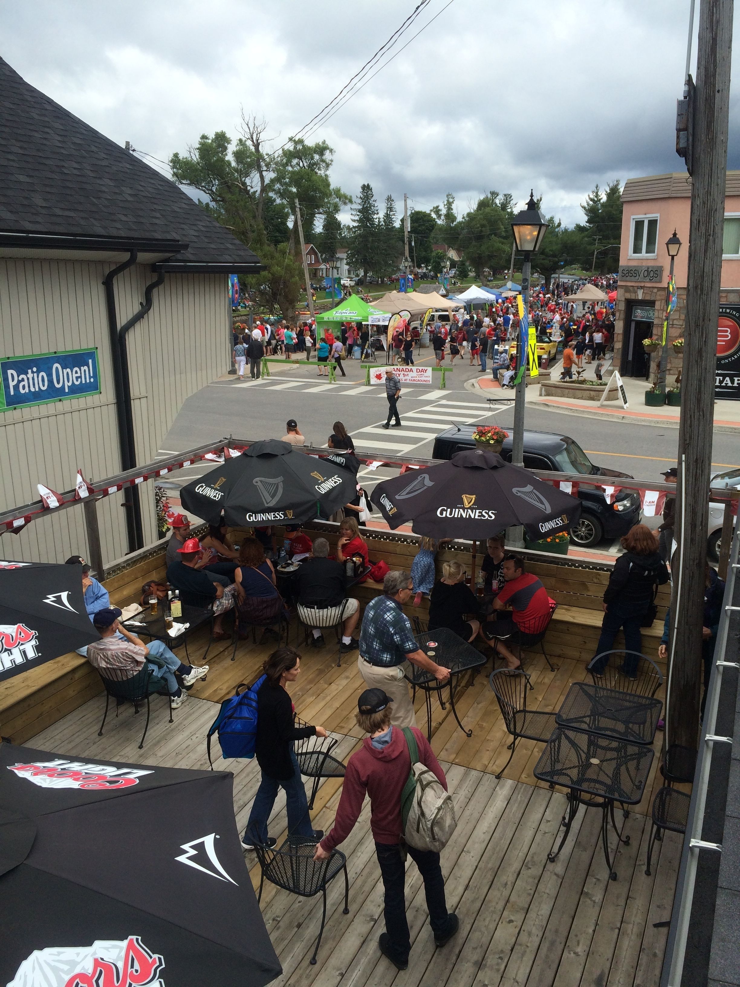 Un espacio al aire libre con mesas y sombrillas, un cartel que indica la disponibilidad de la terraza, y gente en el fondo.