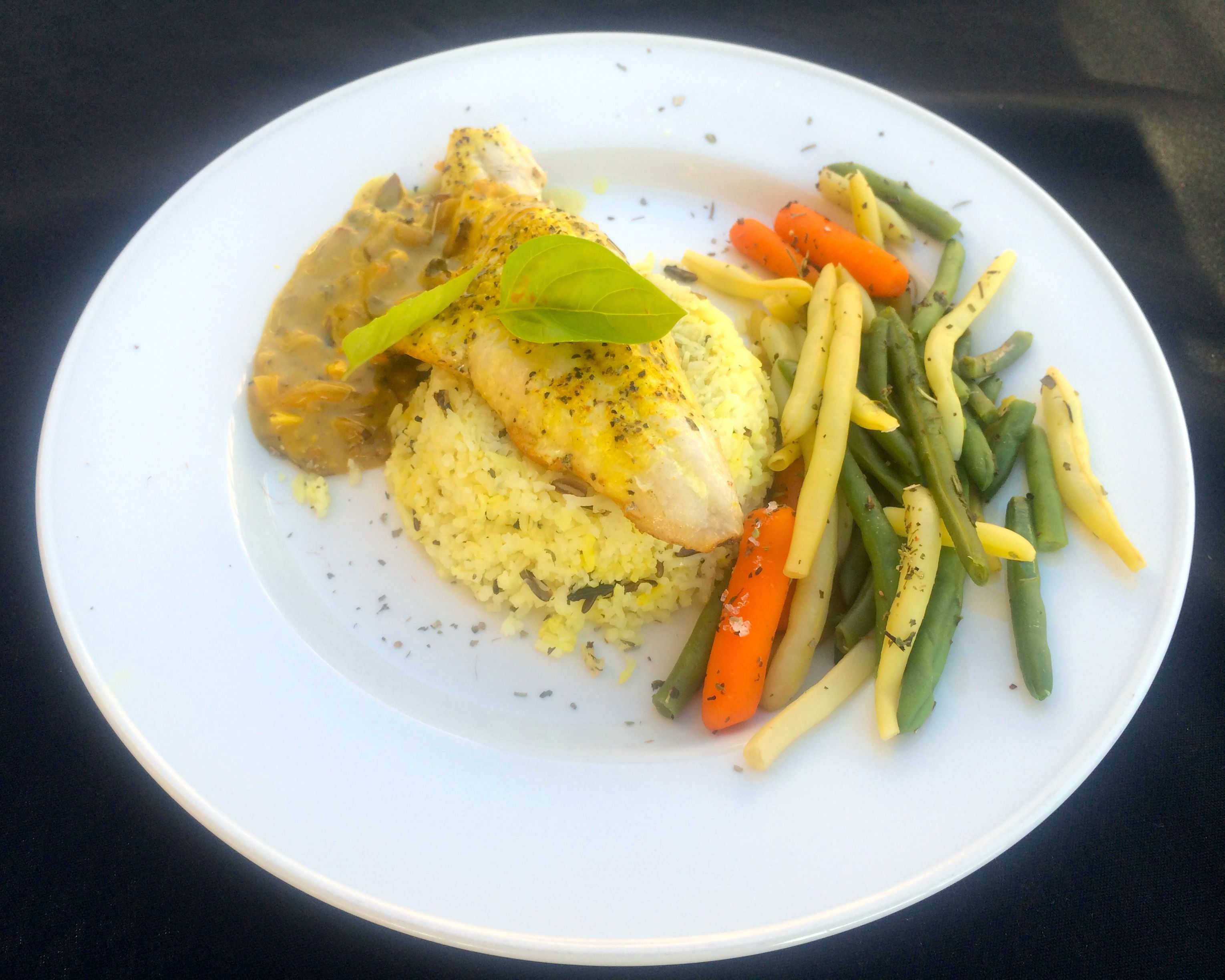 Ein Teller Essen mit Fisch, Reis, Karotten und grünen Bohnen.