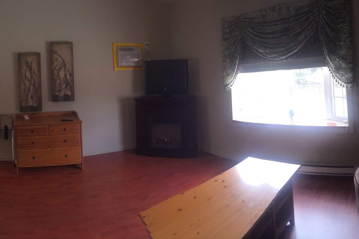 A bedroom with a four-poster bed, a wooden dresser, a television, and a window with curtains.