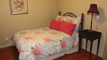 Une chambre à coucher avec une couvre-lit à motifs floraux, une table de chevet en bois et une lampe.