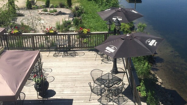 A wooden deck with outdoor furniture, including tables and chairs, overlooking a calm lake with a dock. - Dominion Hotel (Minden Hills)